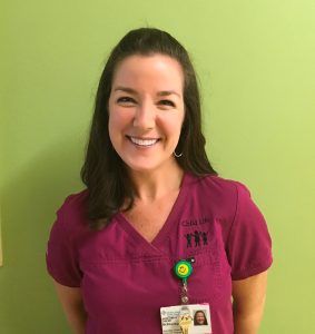 Smiling Caucasian woman with long dark hair and maroon scrubs