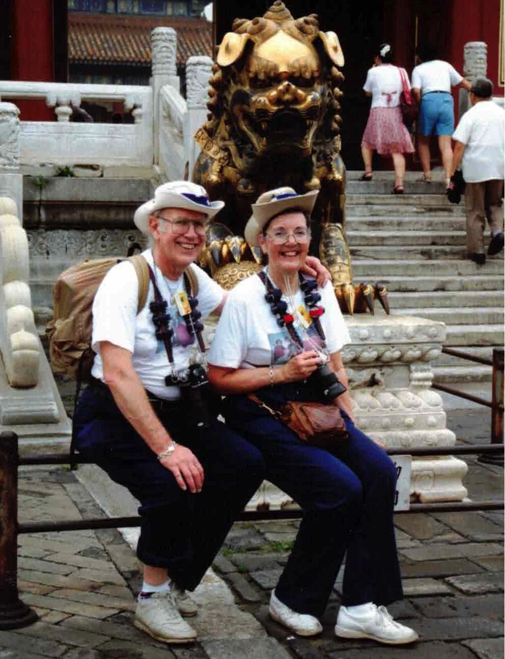 An older Caucasian couple sit with on marble steps with Hawaiian leis around their necks.