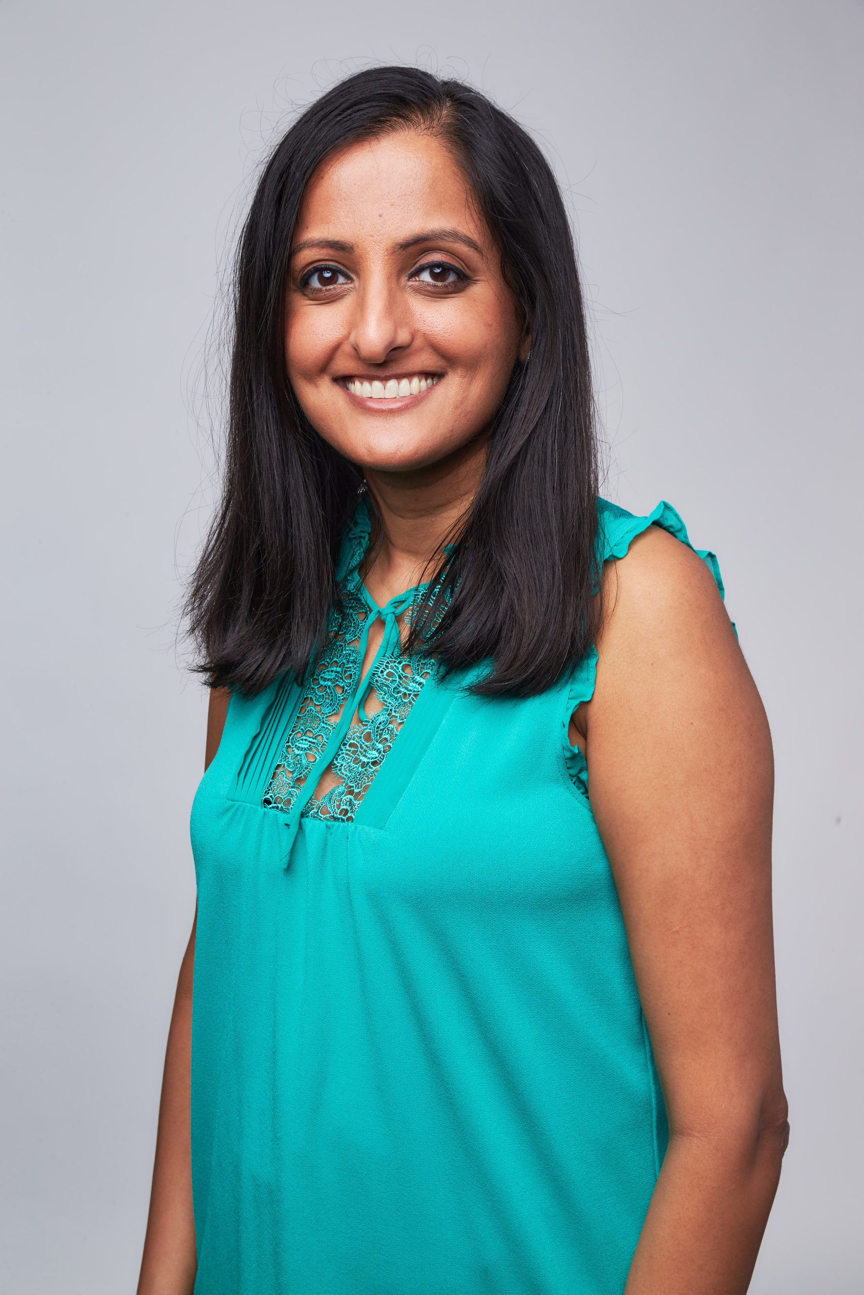 An Indian woman in a teal shirt is smiling.