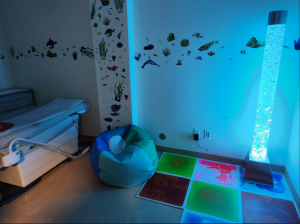 Interior of an exam room that is specially equipped with blue light, fun wall art, and child-friendly furniture. 