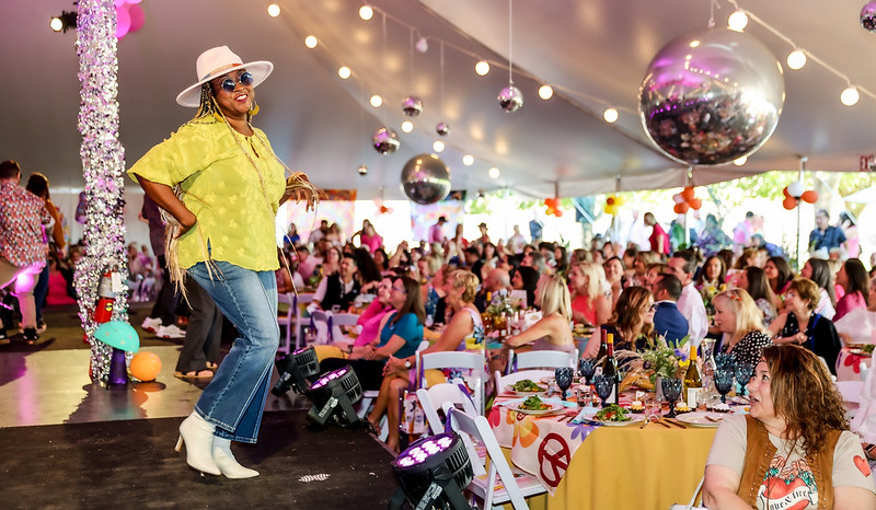 African American woman in vibrant clothing struts on a runway during a cancer fundraising event 