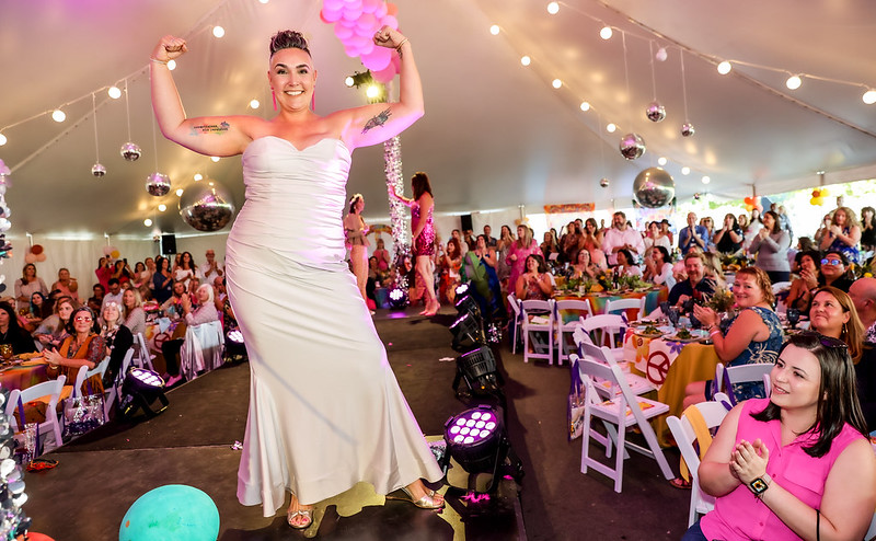 A woman making a muscle pose with her arms struts on a catwalk during a cancer fundraiser