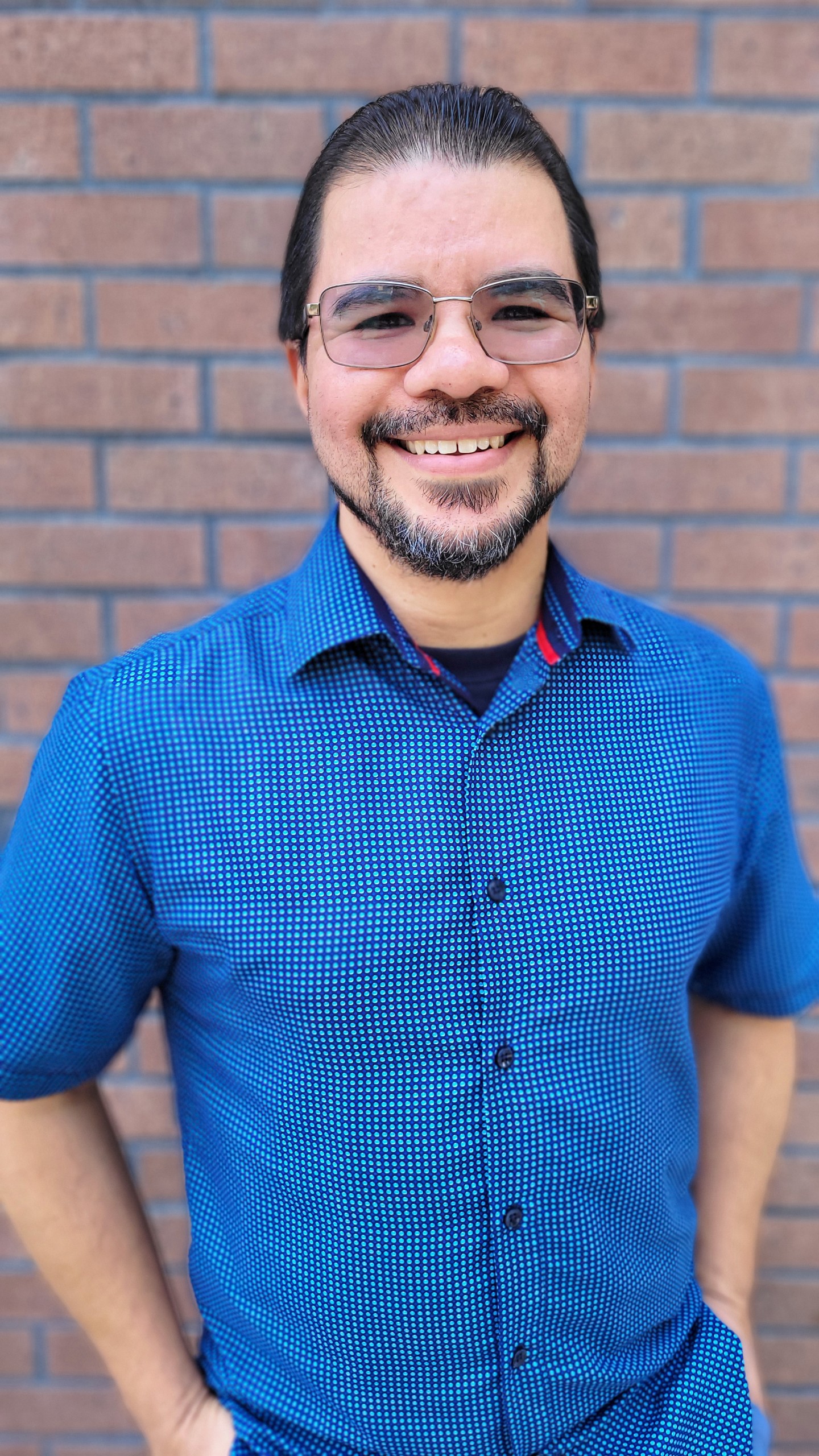 A Hispanic man with glasses and a blue shirt is smiling