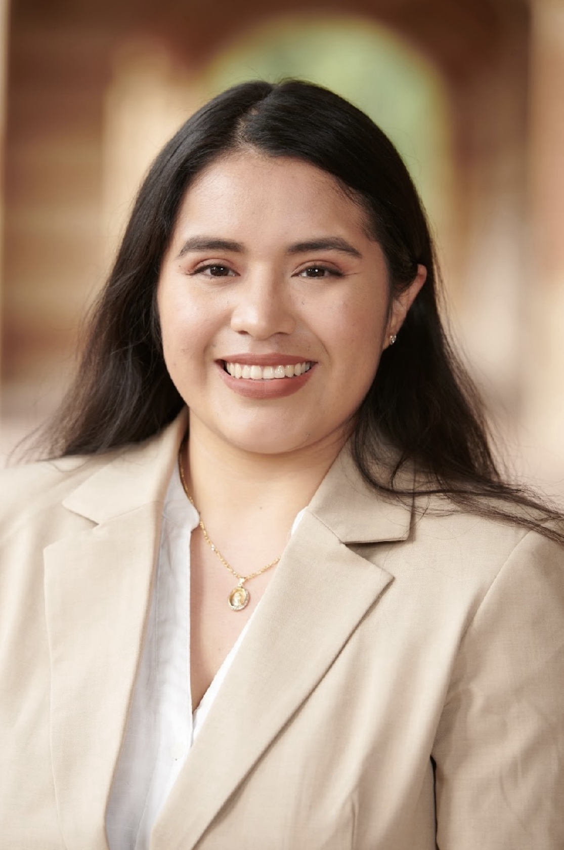 A young Hispanic woman in a tan suit is smiling