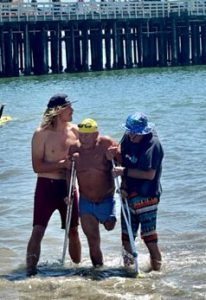 Septuagenarian Bob Duncan completes Santa Cruz Rough Water open swim coming out of the water after race assisted by two men