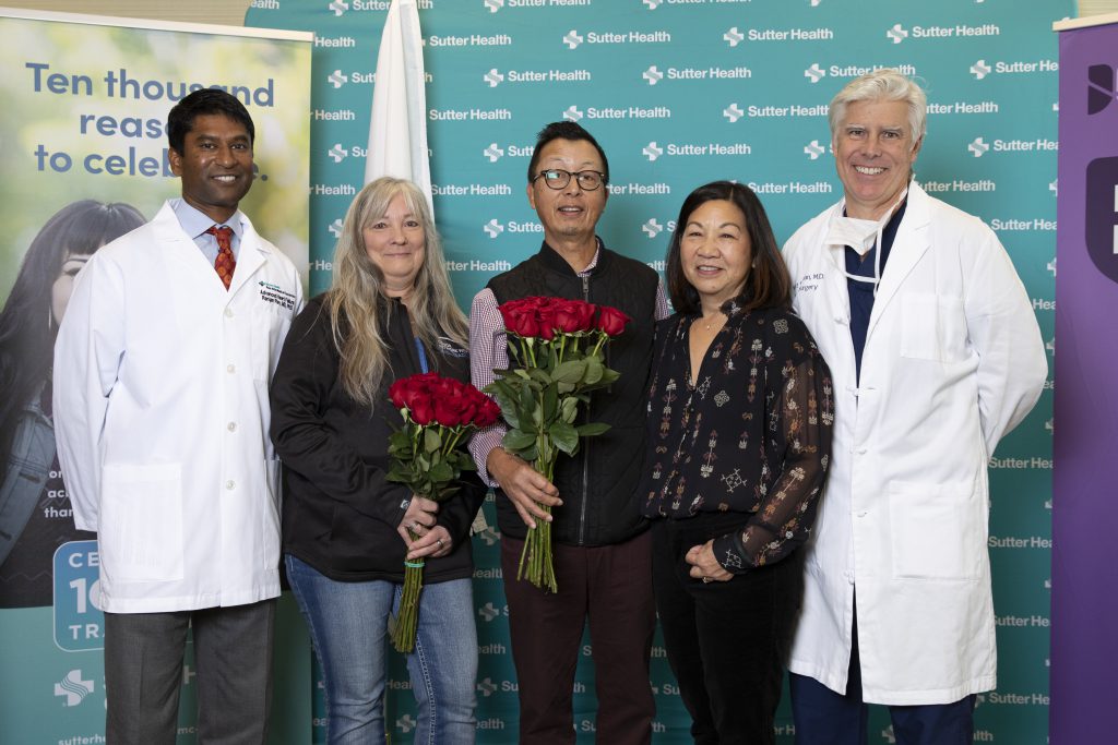 A group of former patients and surgeons gather together for a picture with roses.