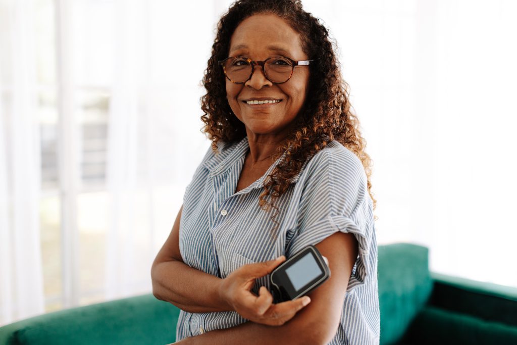 Black woman with glasses and striped shirt places a continuous glucose monitor on her arm