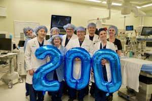 Surgical team in an operating room wearing surgical gowns hold 2-0-0- balloons to celebrate a recent procedure milestone
