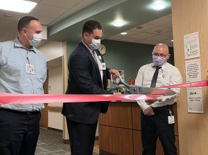 Photo of a ribbon cutting featuring 3 people and big scissors. 