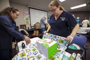 Two female nurses in navy blue scrubs wrapping presents