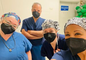 A group of two doctors and two nurses take a selfie while in surgical scrubs and masks