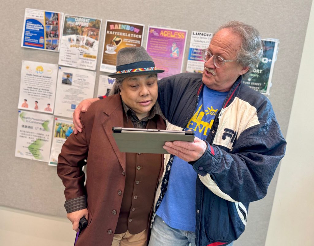Two seniors from San Francisco's Tenderloin neighborhood embrace while looking at an iPad