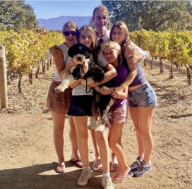 A Caucasian family of father, mother and three daughters pose in a vineyard
