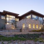 A modern building with numerous glass windows and a stone facade sits on a hillside at twilight