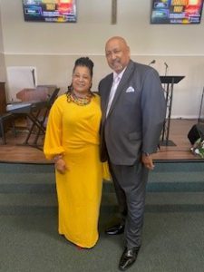 Gwen McCauley in a long yellow gown and her husband Pastor Joseph McCauley