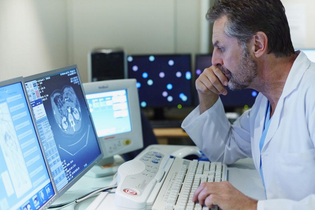 Side view of male doctor examining CT scan in control room at hospital