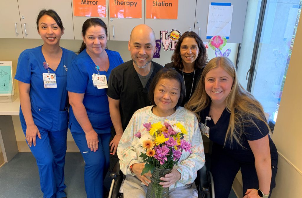 Asian woman in wheelchair is surrounded by her hospital rehabilitation care team
