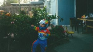 Young child dressed in a race car driver outfit plays in his home's backyard