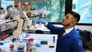 Latino man in lab with goggles reaching for equipment