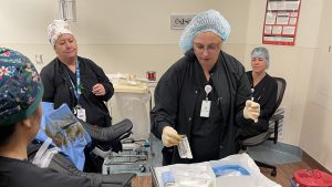 Nurse practices placing a catheter while other nurses watch inside an operating room