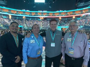 Group shot of four men standing and smiling at camera.