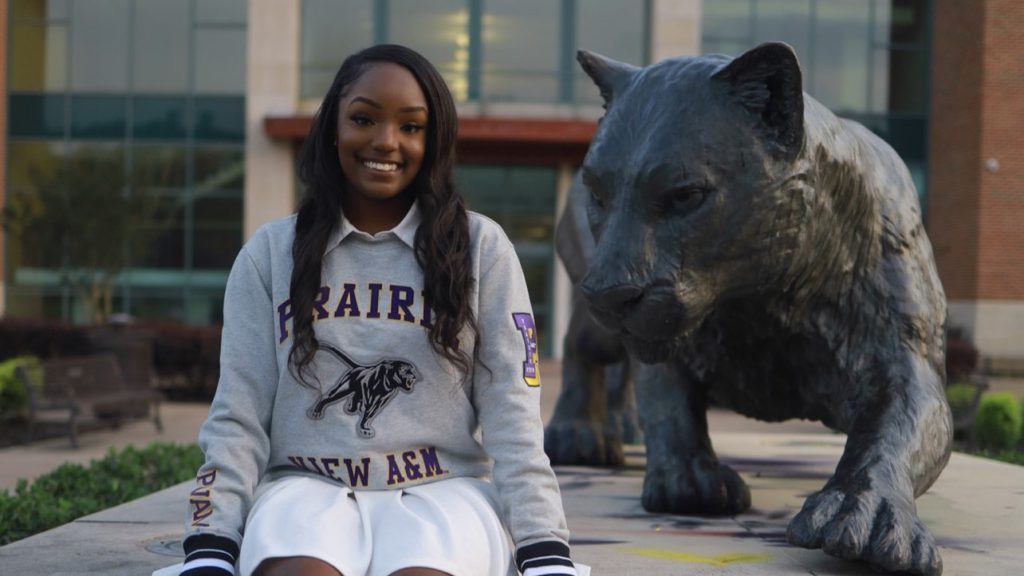 Black woman in college sweatshirt poses next to college mascot