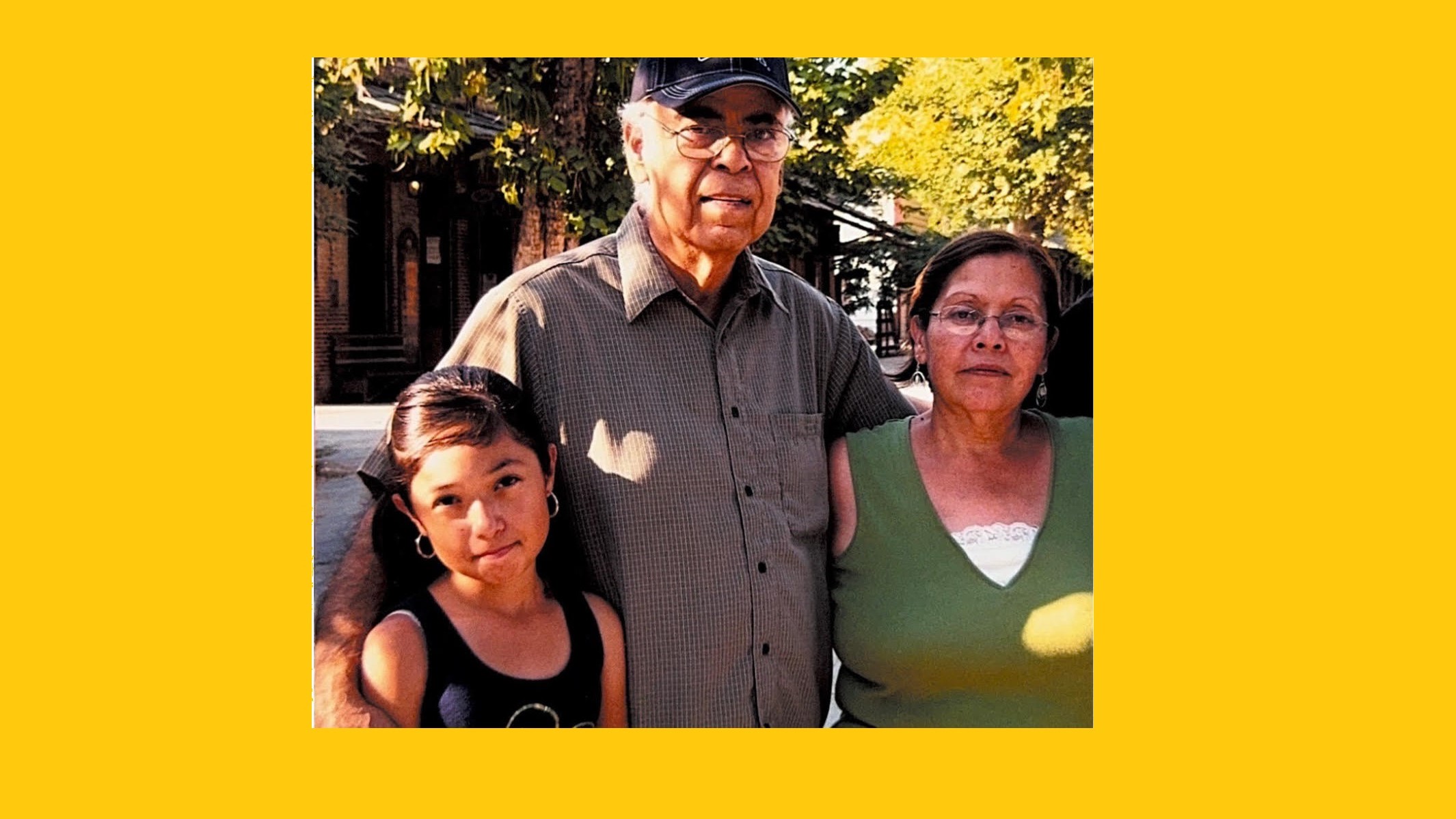 Young Latina girl poses for a photo with her grandparents with fall foliage in the background