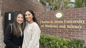 Two Latina woman pose in front of university monument sign