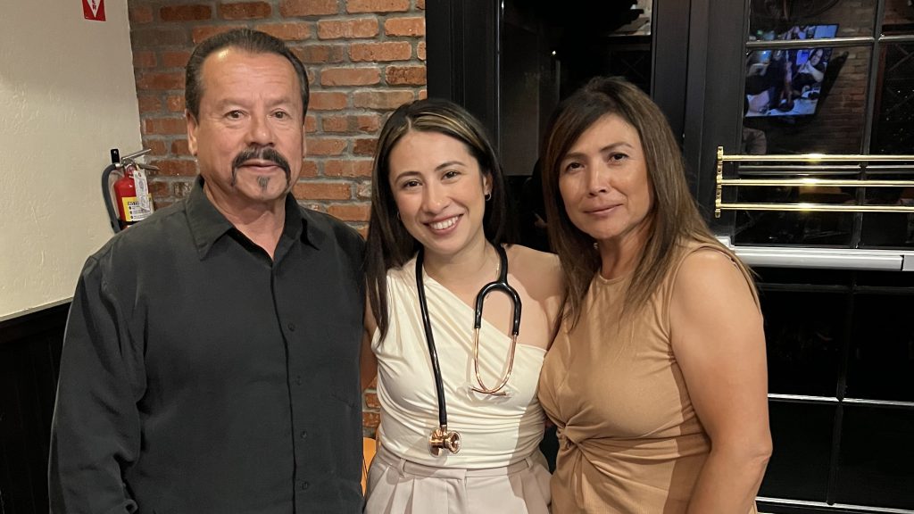Latino family of father, daughter wearing a stethoscope and mother pose in a restaurant for photo