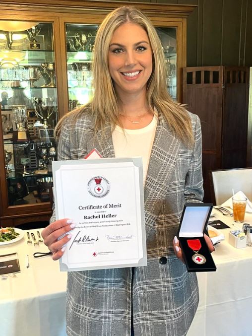 A woman in a plaid blazer and jeans holds up a Red Cross medal and award certificate