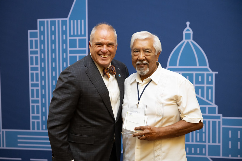 Two men posing for a photo with an illustration of a city scape behind them