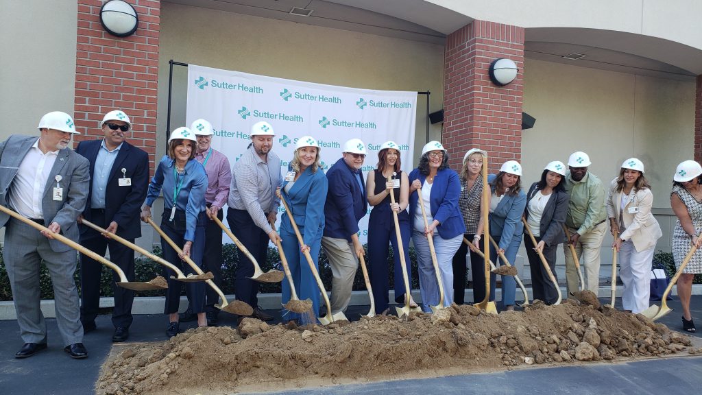 Numerous adults in hard hats shoveling ceremonial dirt in a parking lot