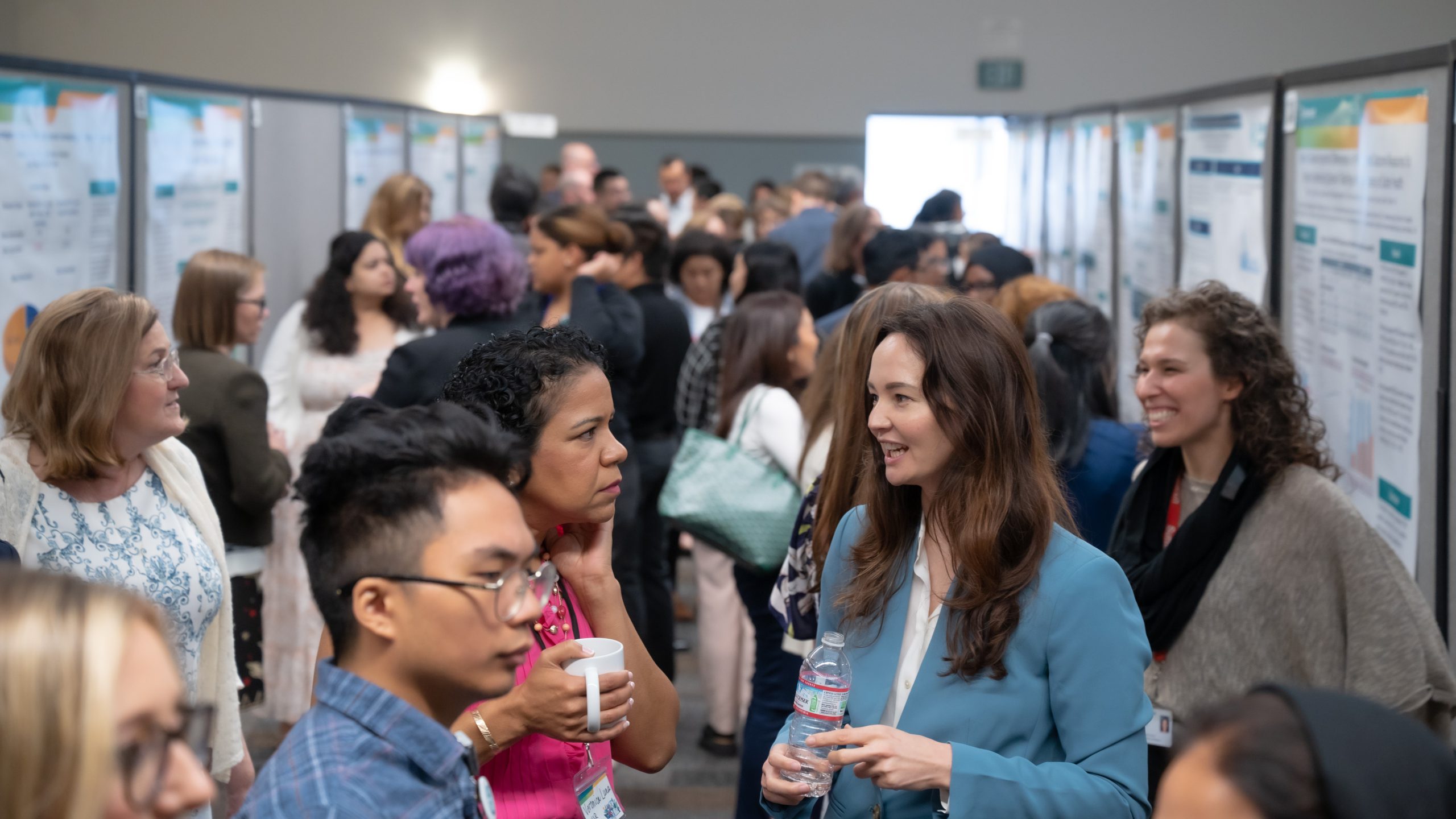 Crowd of people stand in hallway where research posters are on each side of the wall