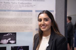 Southeastern Asian woman poses in front of research poster at conference