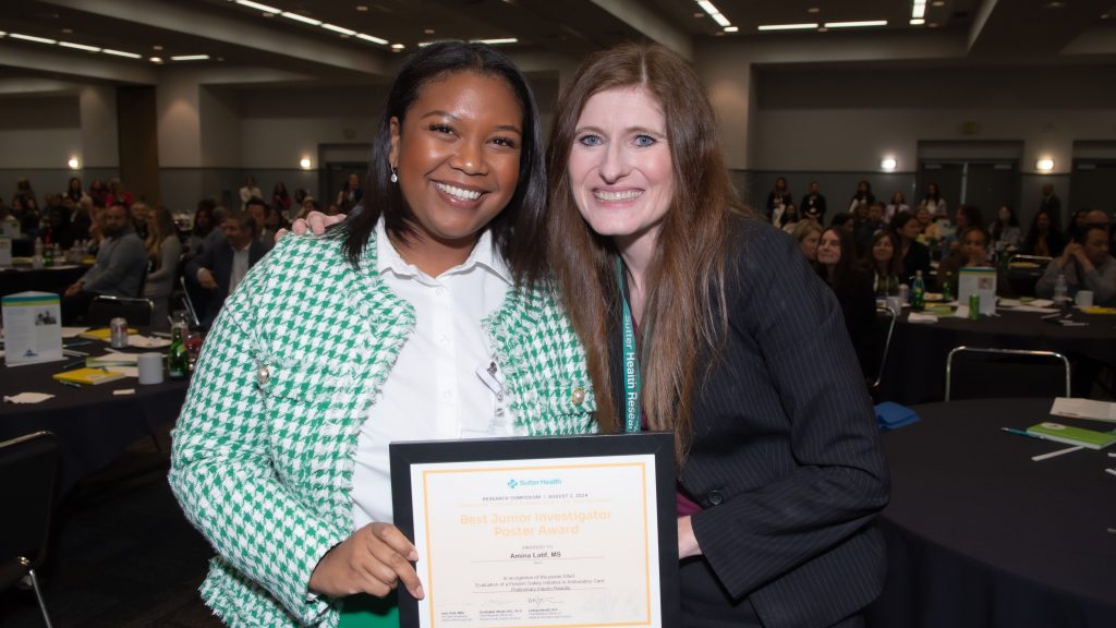 A black and white woman pose with an plaque award with numerous people in the background sitting at circular tables