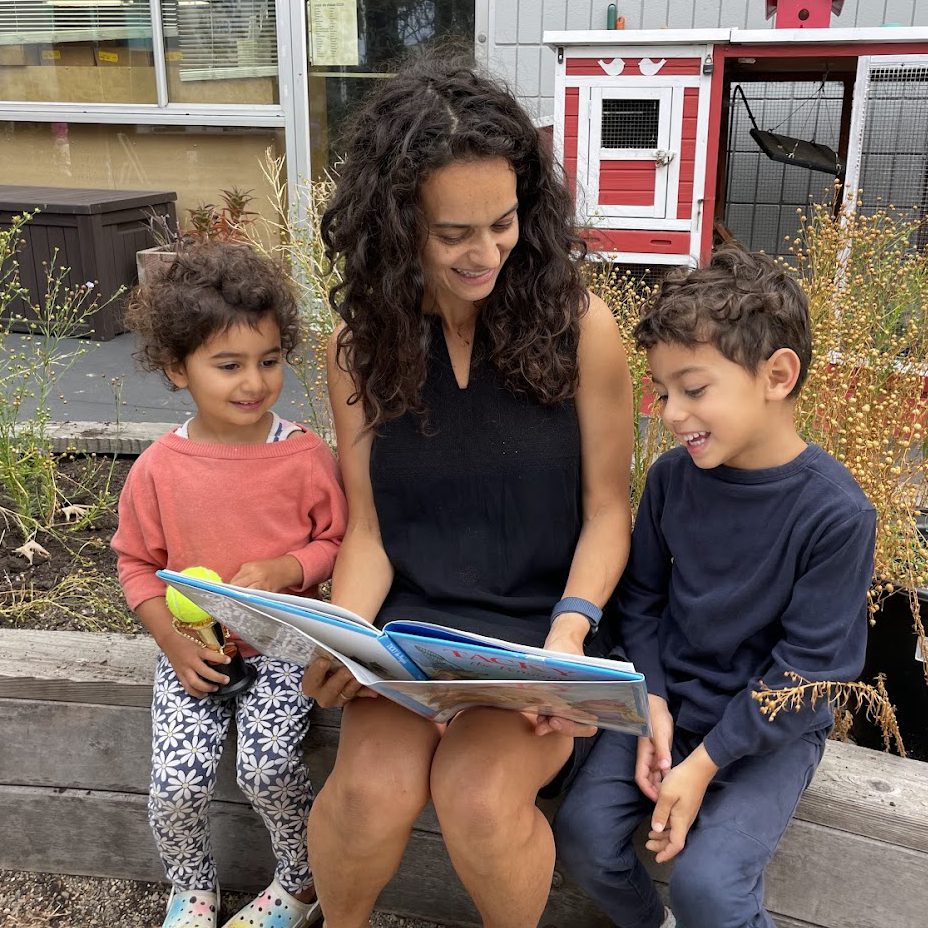 A mother reads on a bench to her two young children