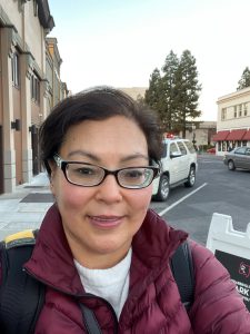 Portrait of woman with dark hair, glasses and maroon puffy jacket