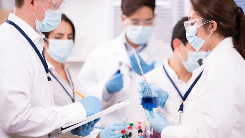 Team of medical researchers in lab and wearing lab coats and surgical masks