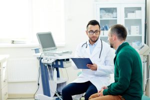 Middle-aged bearded patient having consultation with highly professional physician at modern office, they discussing diagnosis and possible treatment