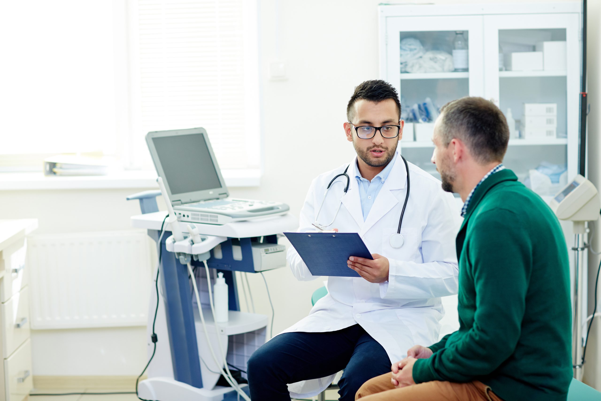 Middle-aged bearded patient having consultation with highly professional physician at modern office, they discussing diagnosis and possible treatment