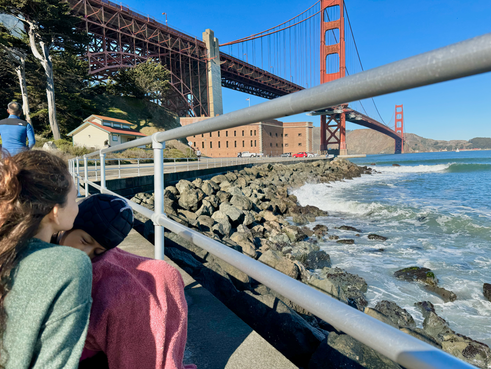 Two young women stand beneath the Golden Gate Bridge