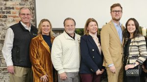 Group of adults pose for a photo with projector screen and a brick wall behind them