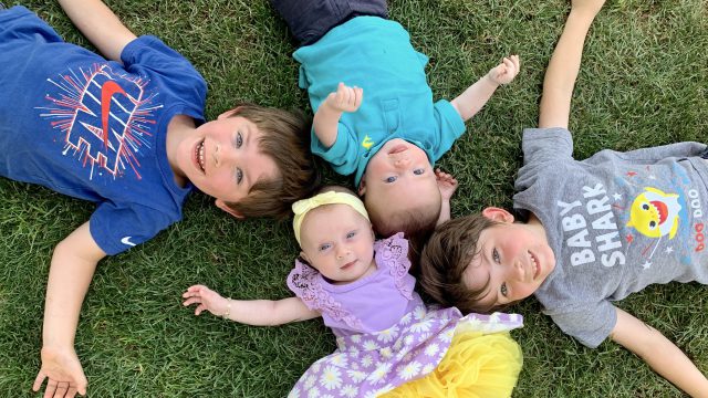 Four children lay on the grass in a circle with their heads meeting in the middle