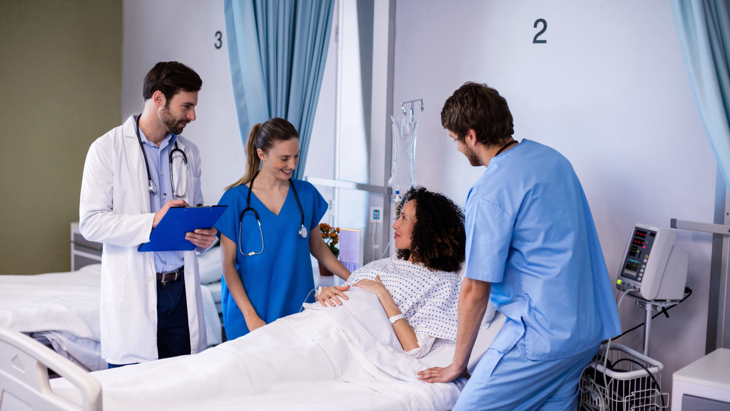 Physicians consult with pregnant woman in hospital bed