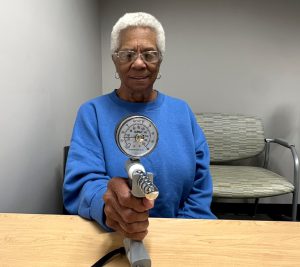 photo of a patient participating in grip strength test wearing a blue sweater with white hair