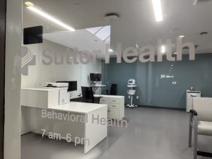 a photo of a medical office waiting area as seen looking through the entrance window with Sutter Health logo on the glass