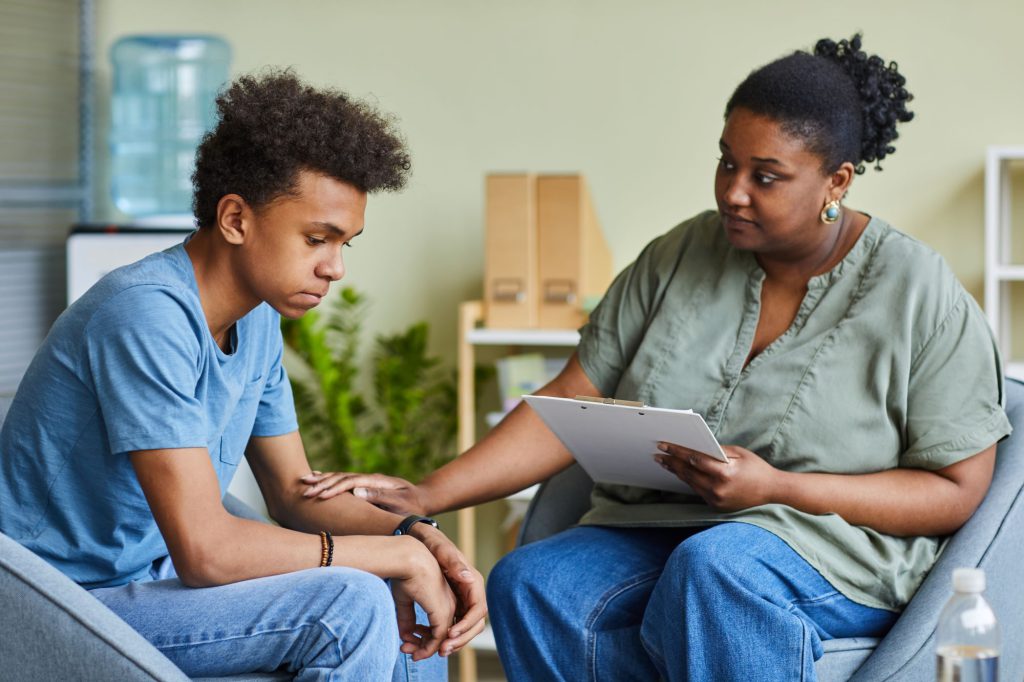 African psychologist supporting depressed teenage boy feeling guilty about behavior during therapy at office