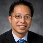 Doctor posing for headshot, in dark blazer with blue tie