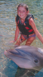 Young Cayla in the ocean with a dolphin.