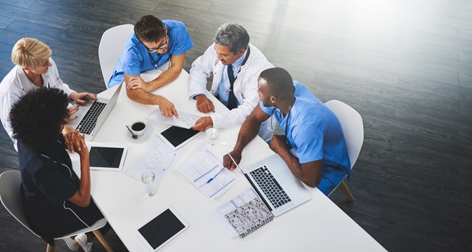 Team of medical workers sitting and meeting with laptops around table. Doctors and staff discussing papers and test results. Healthcare experts handling daily tasks and duties.
